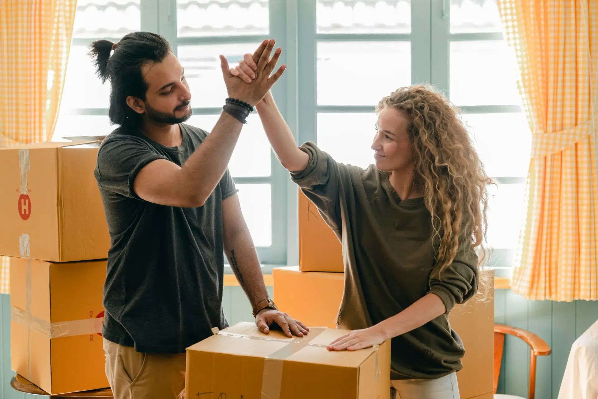 Ein Paar gibt sich ein High-Five während des Umzugs in ihr neues Zuhause, dank erfolgreichem Bausparen und einer gut geplanten Baufinanzierung.